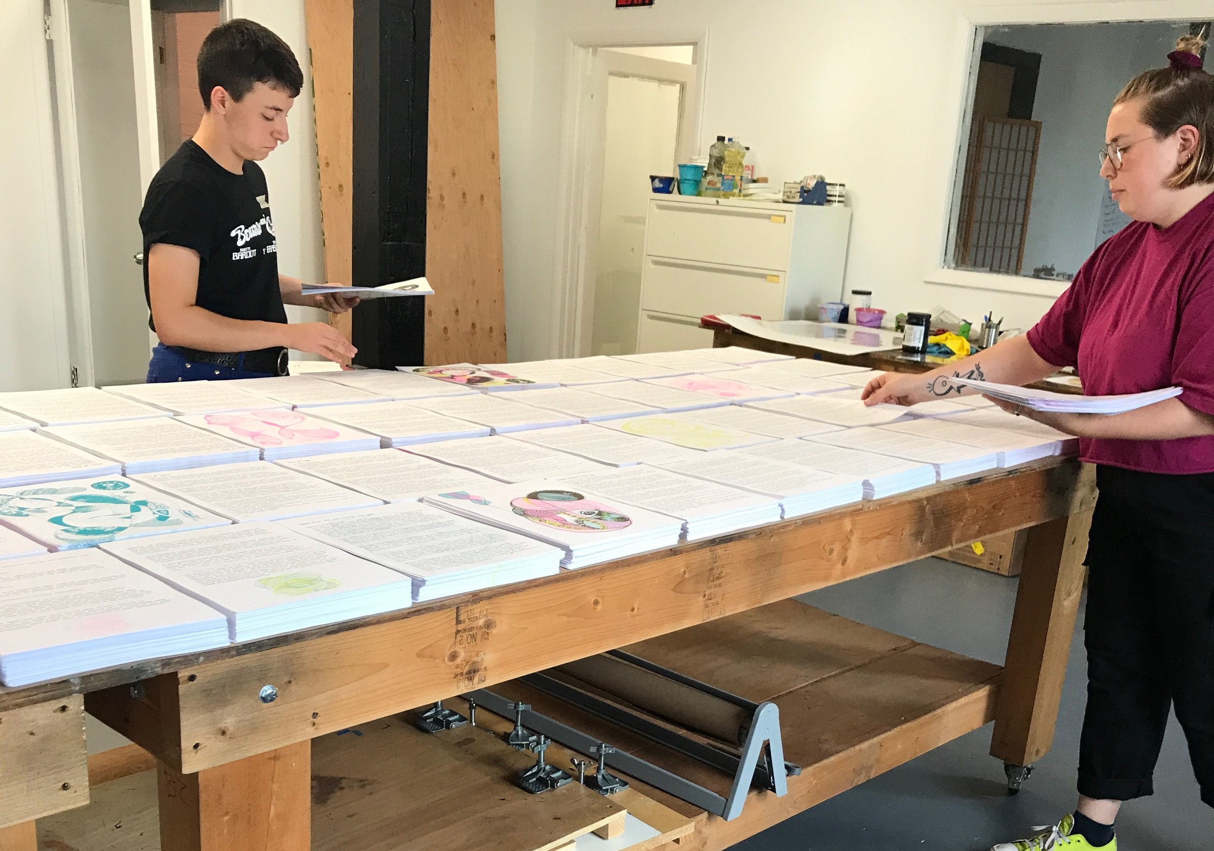 two white people standing at a huge table covered with stacks of risograph printed pages