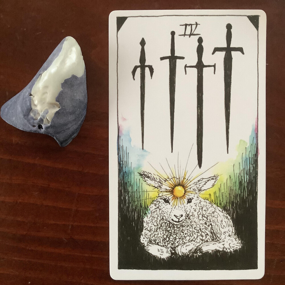 a lamb with a radiating sun at their third eye sits at the base of the card, 4 downward-pointing swords hover above