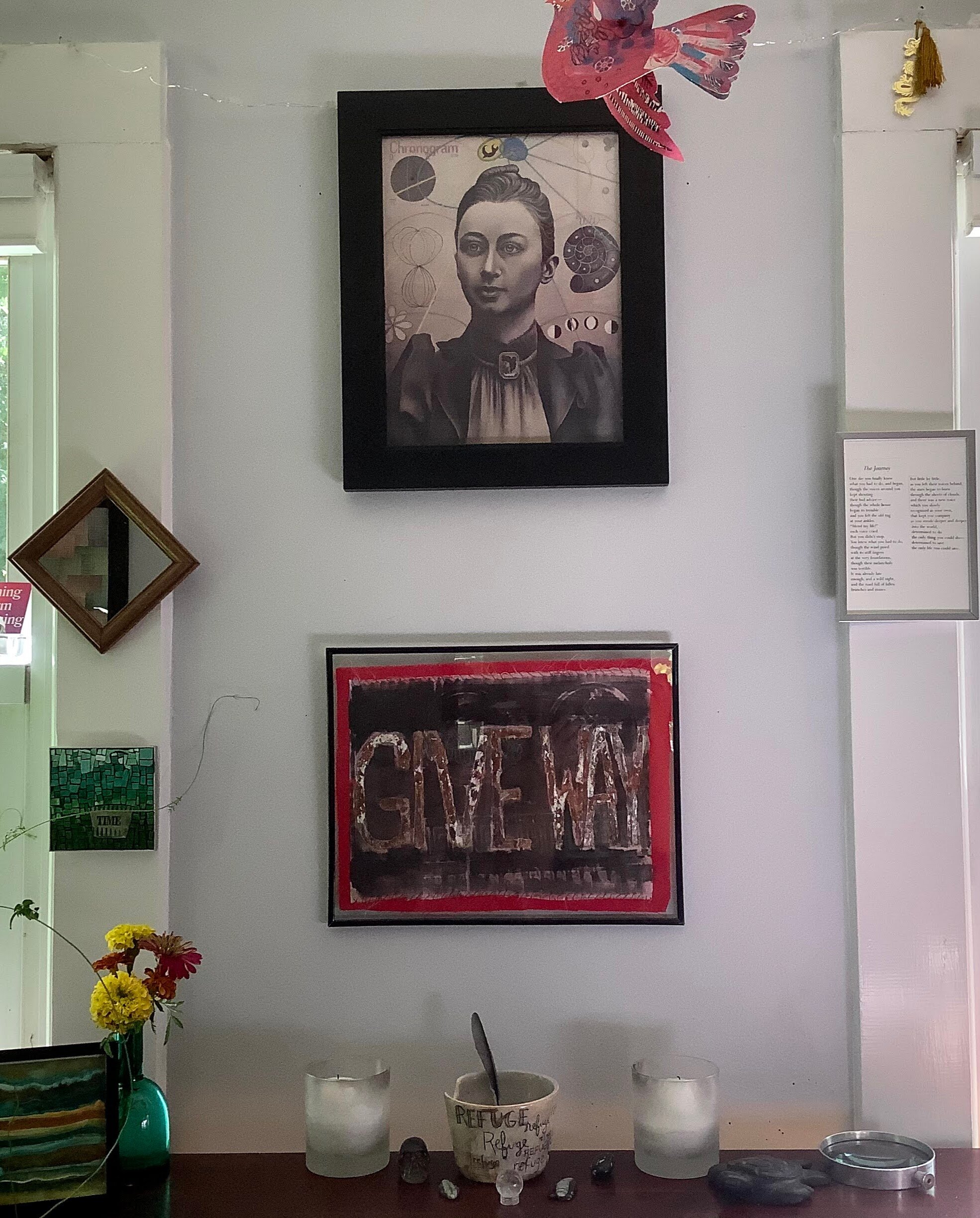 an altar on a desk that includes fresh flowers, candles an incense bowl, an artwork that says Give Way