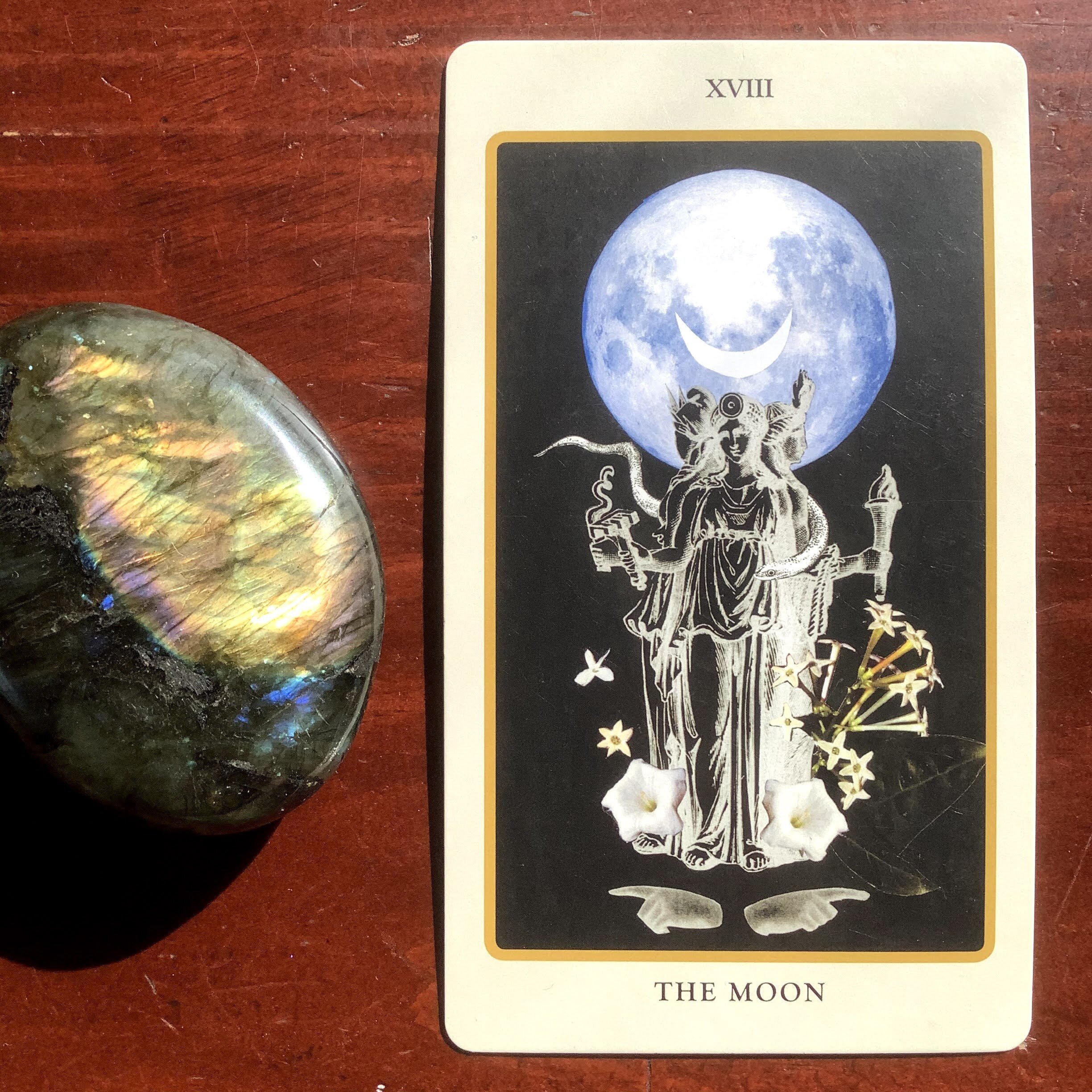 Labradorite stone alongside a tarot card depicting a black and white triple goddess Hekate, a blueish full moon and white flowers