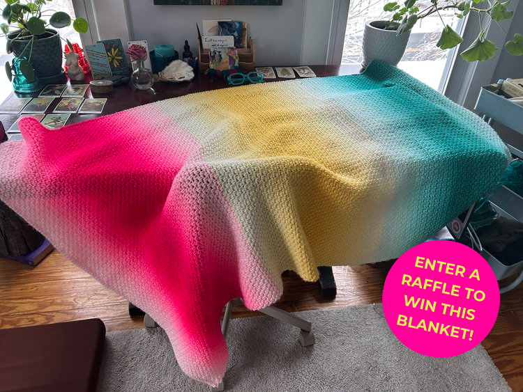 Enter a raffle to win this blanket, with a pink, yellow and teal crocheted blanket draped over a desk