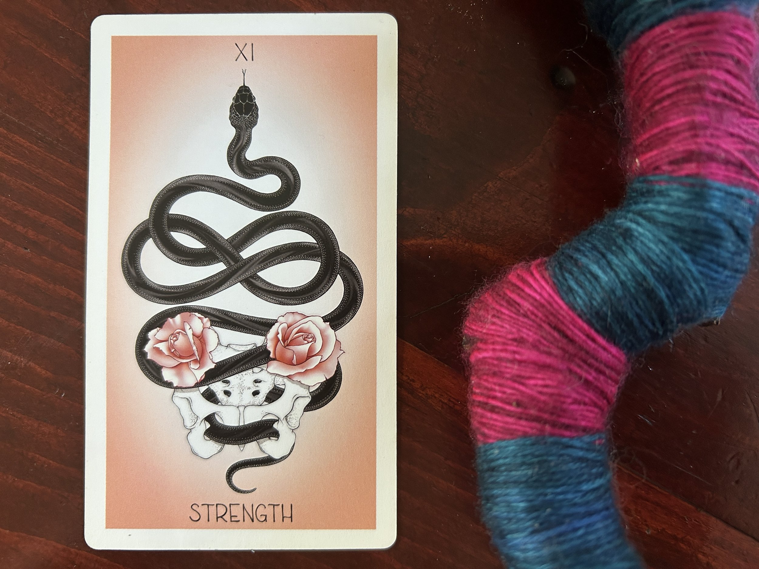 a strength tarot card showing a snake threading its body through the holes of a pelvis with two blooming roses