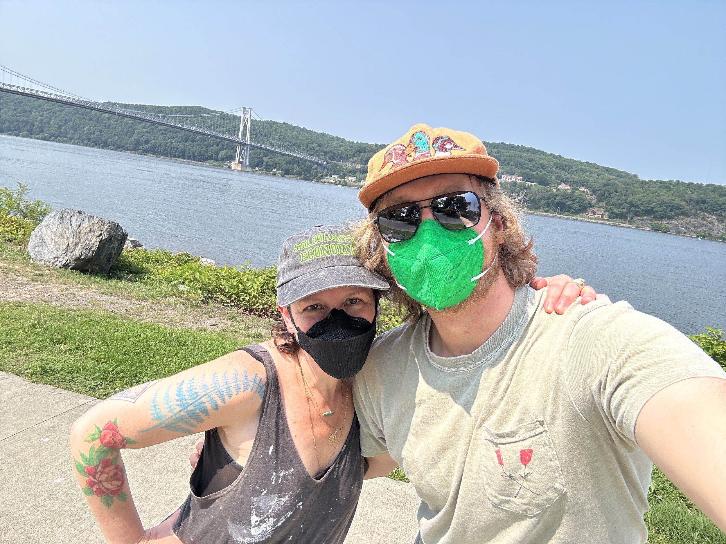 two white people wearing hats and masks in front of a river and bridge