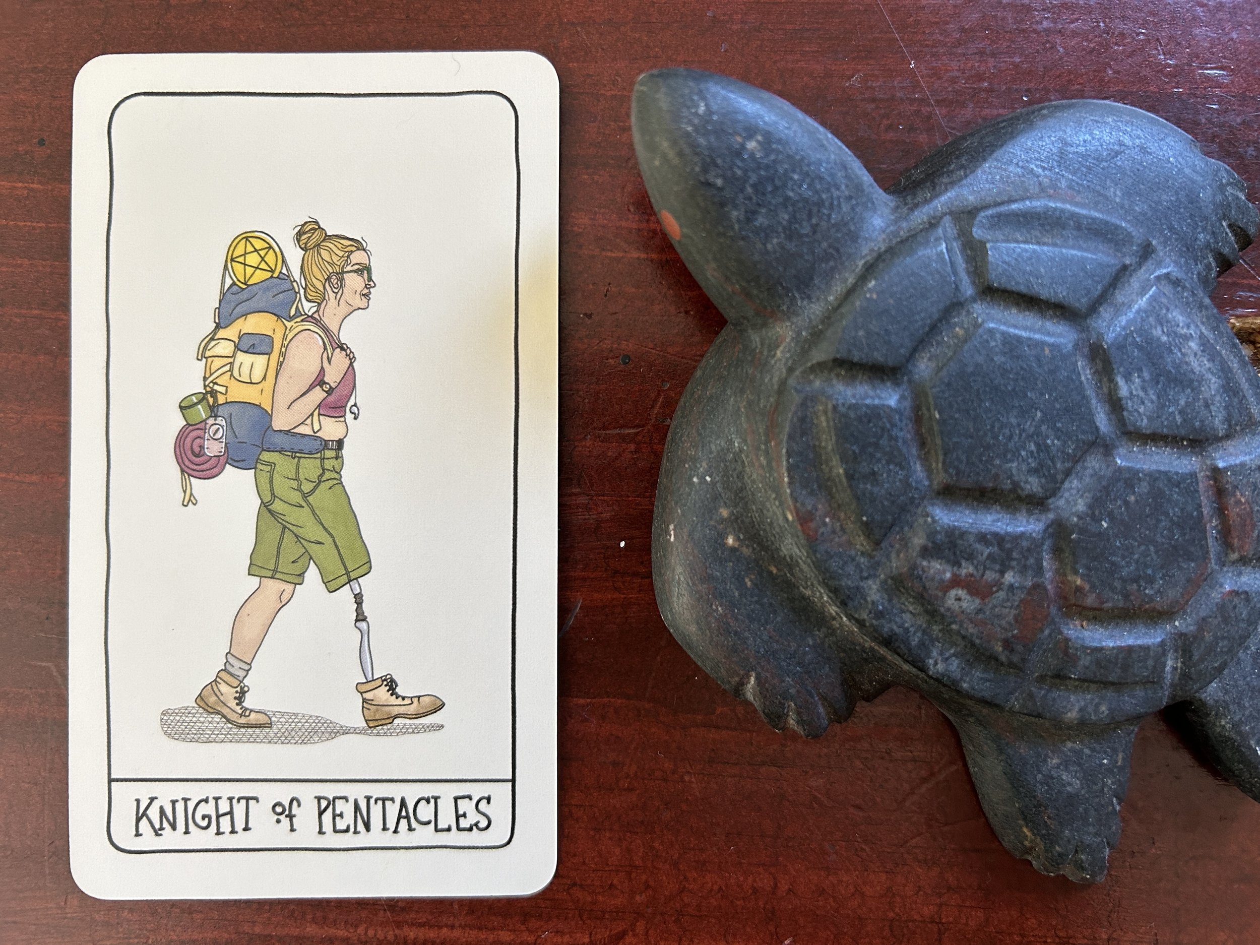 a white person walking in profile with a big hiking backpack, hiking boots and one artificial leg next to a turtle sculpture