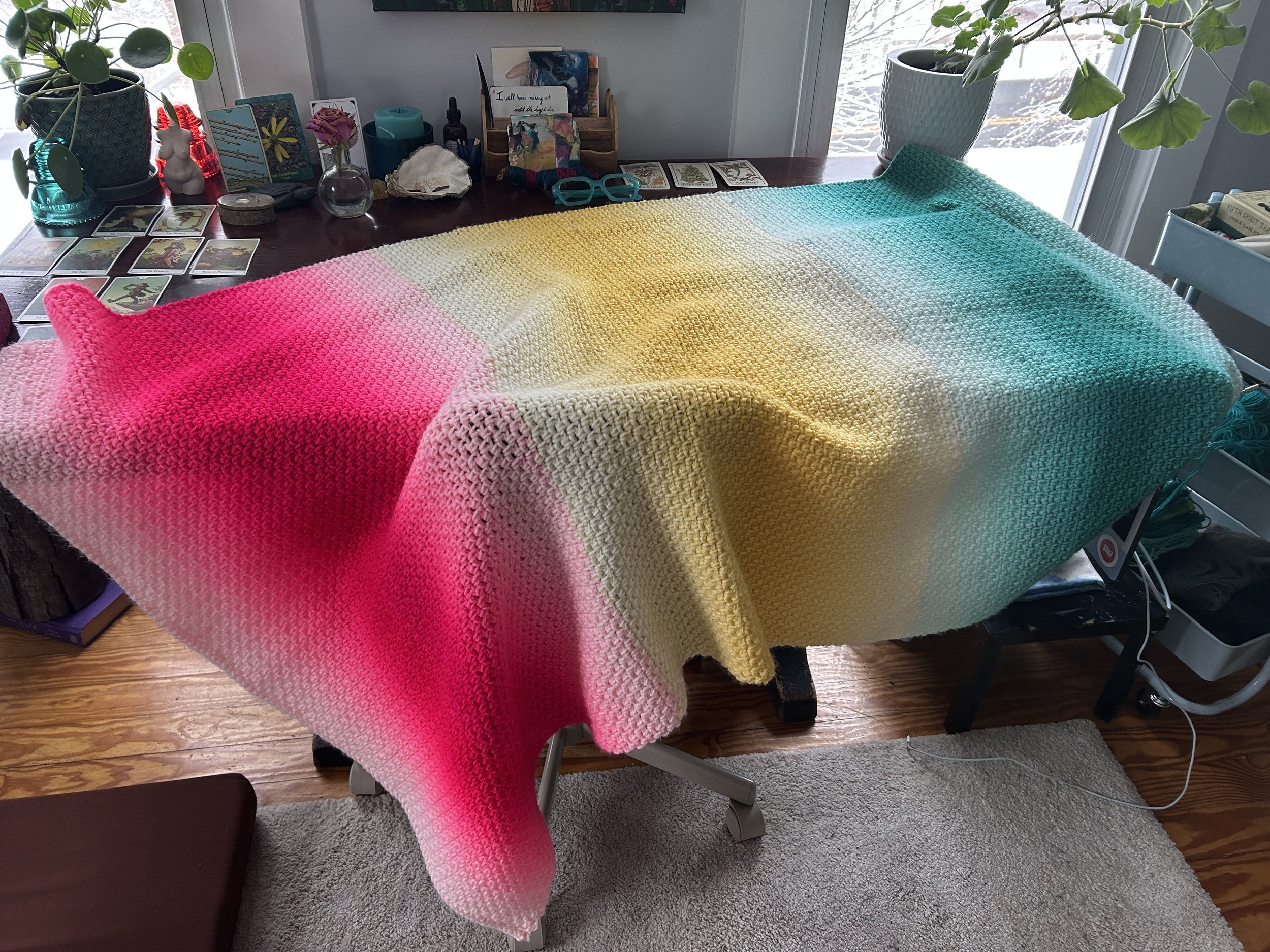 pink, yellow and teal crocheted blanket draped over a desk