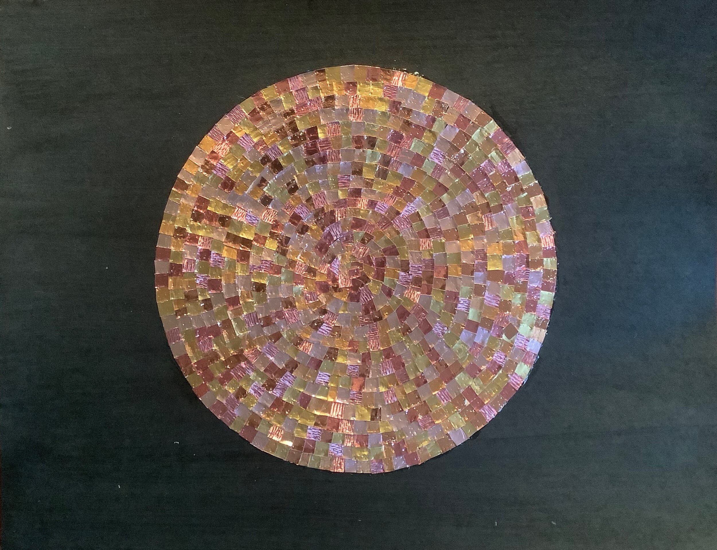 a multi-toned pink circle made out of tiny squares of shiny foil paper against a black ground