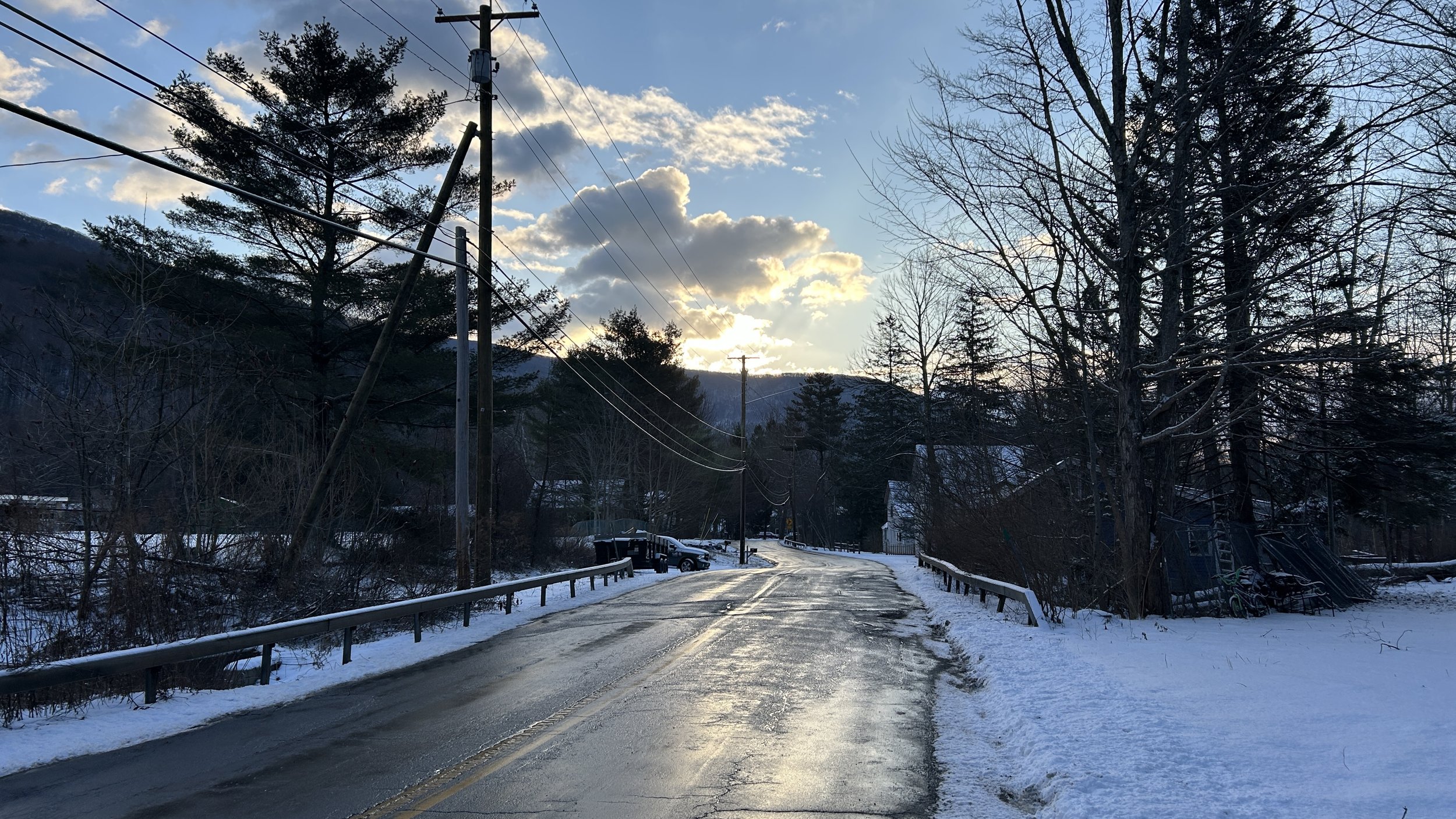 sunrise over a two-lane road flanked by tall trees and snow on the ground