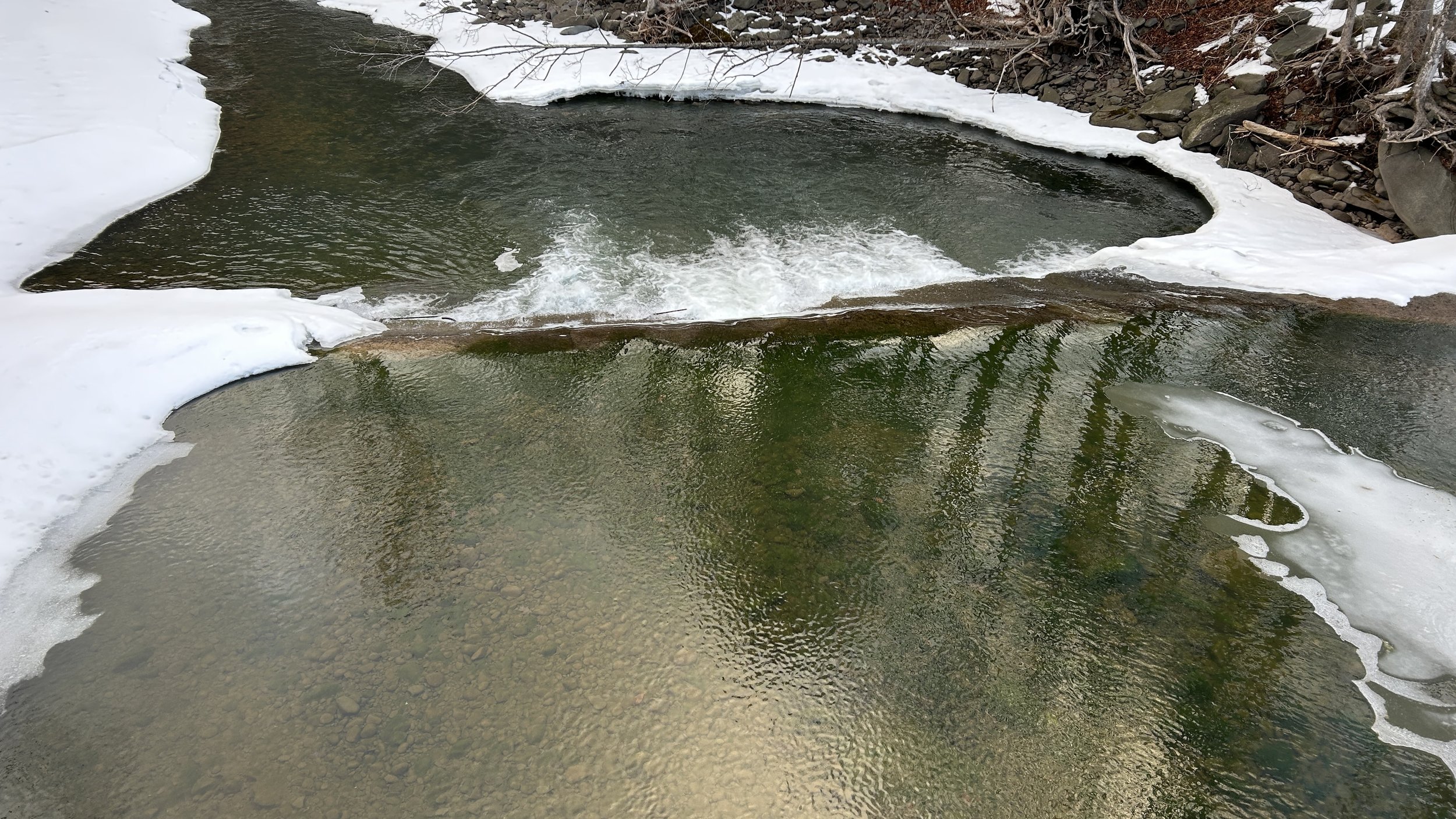 the rippled surface of a creek with snow and ice along the edges