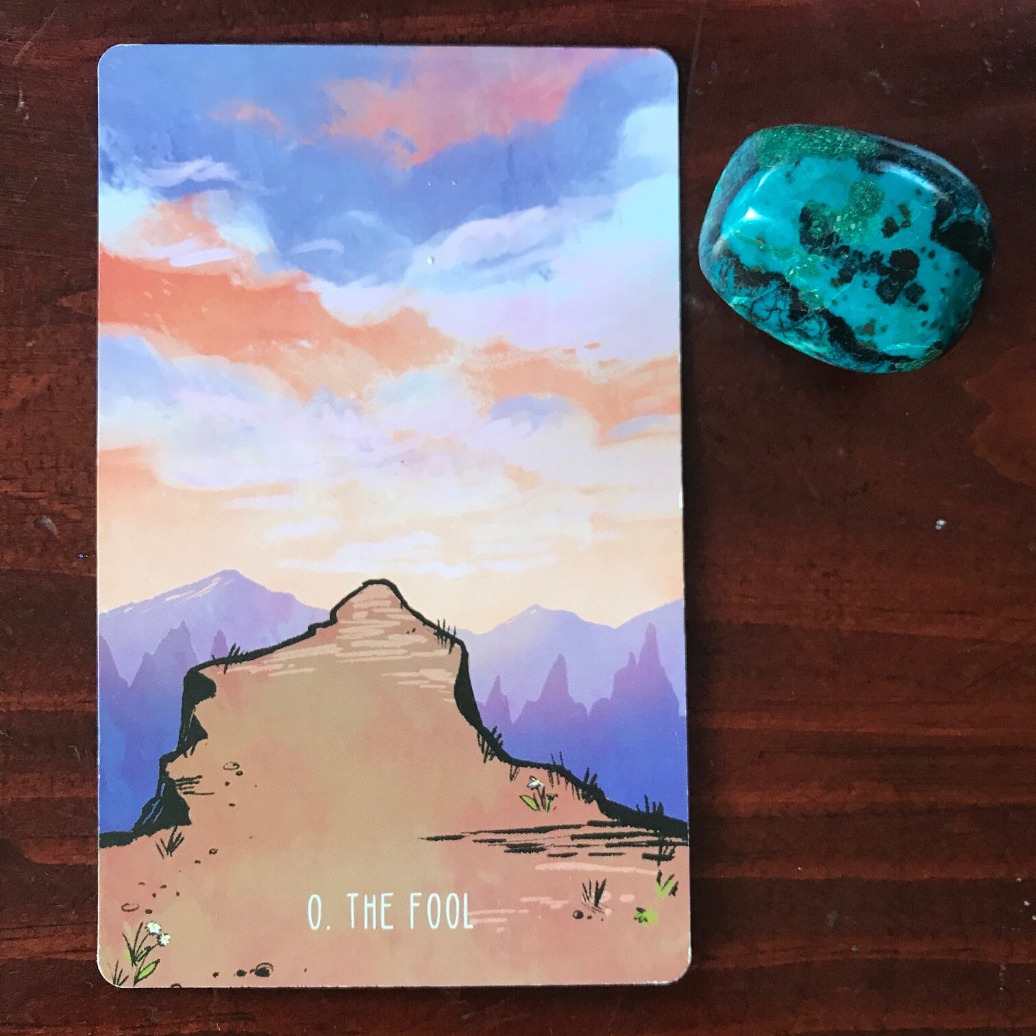 a tarot card showing a path that seems to drop off into an abyss with purple mountains and a peachy sky in the distance