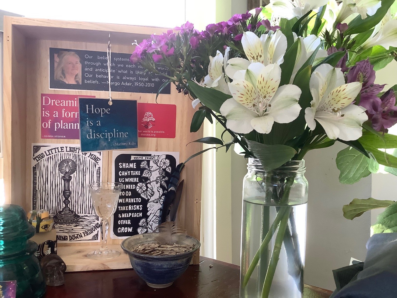 a work altar on a desk that includes a vase of flowers, incense bowl and a light wood box lined with inspirational postcards that say Hope is a discipline and Dreaming is a form of planning
