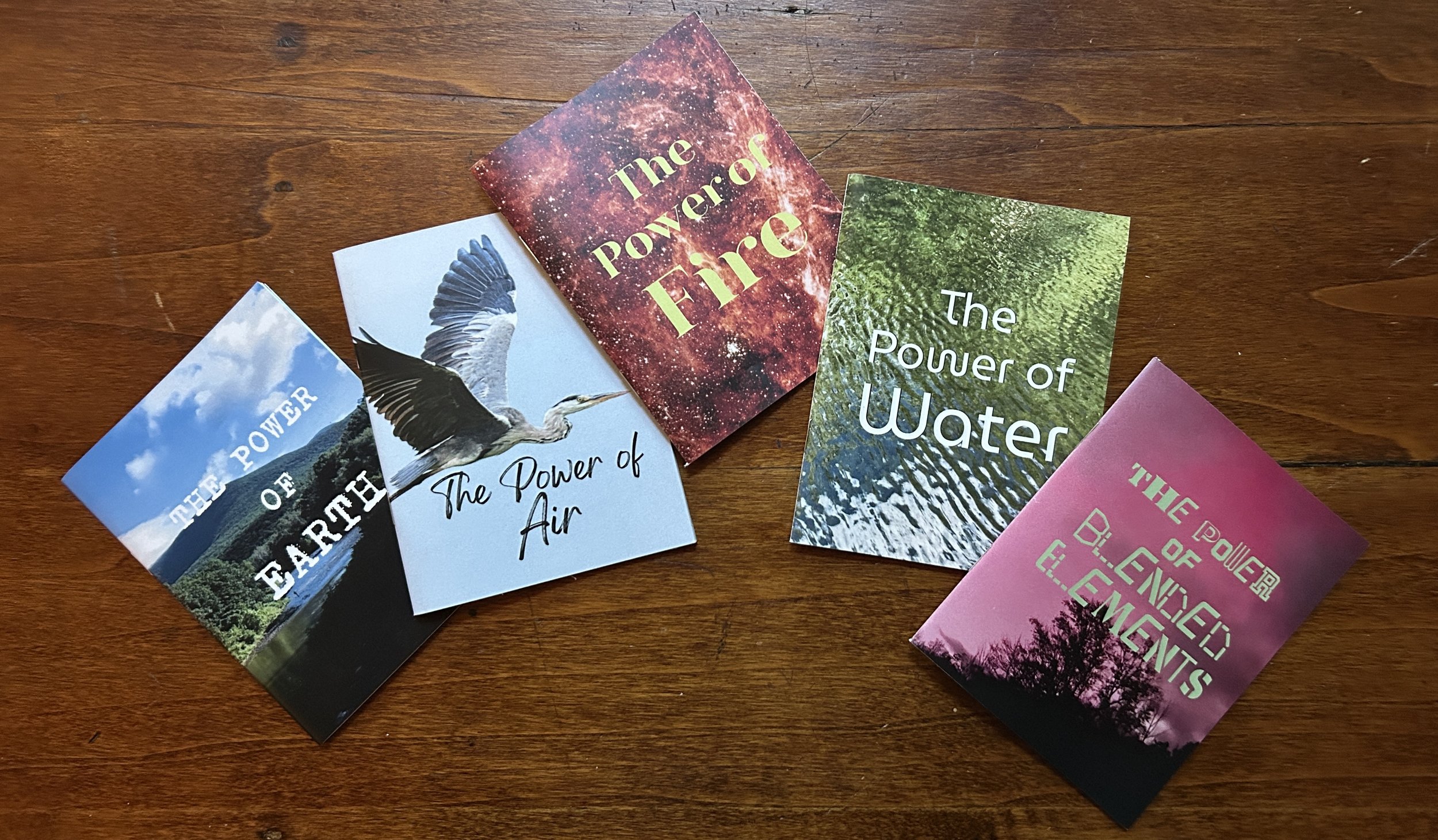 5 quarter-page zines against a wood surface: the power of earth, the power of air, the power of fire, the power of water, and the power of blended elements