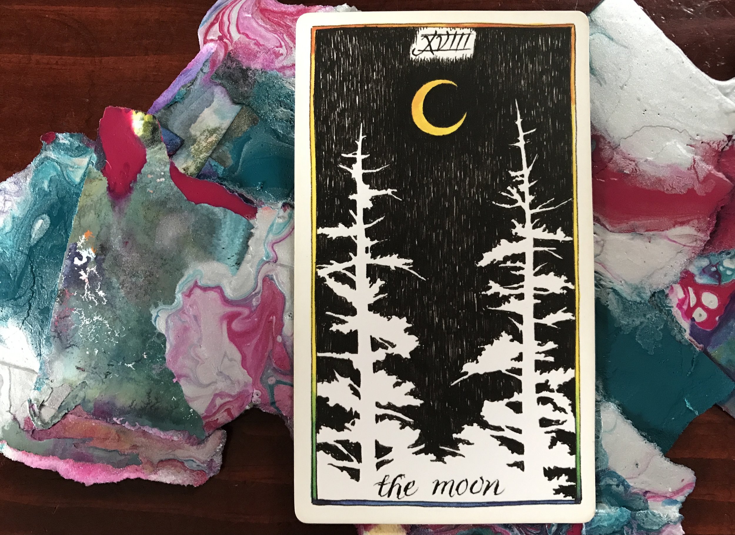 a black and white tarot card against a pile of abstract paintings against a dark wood surface