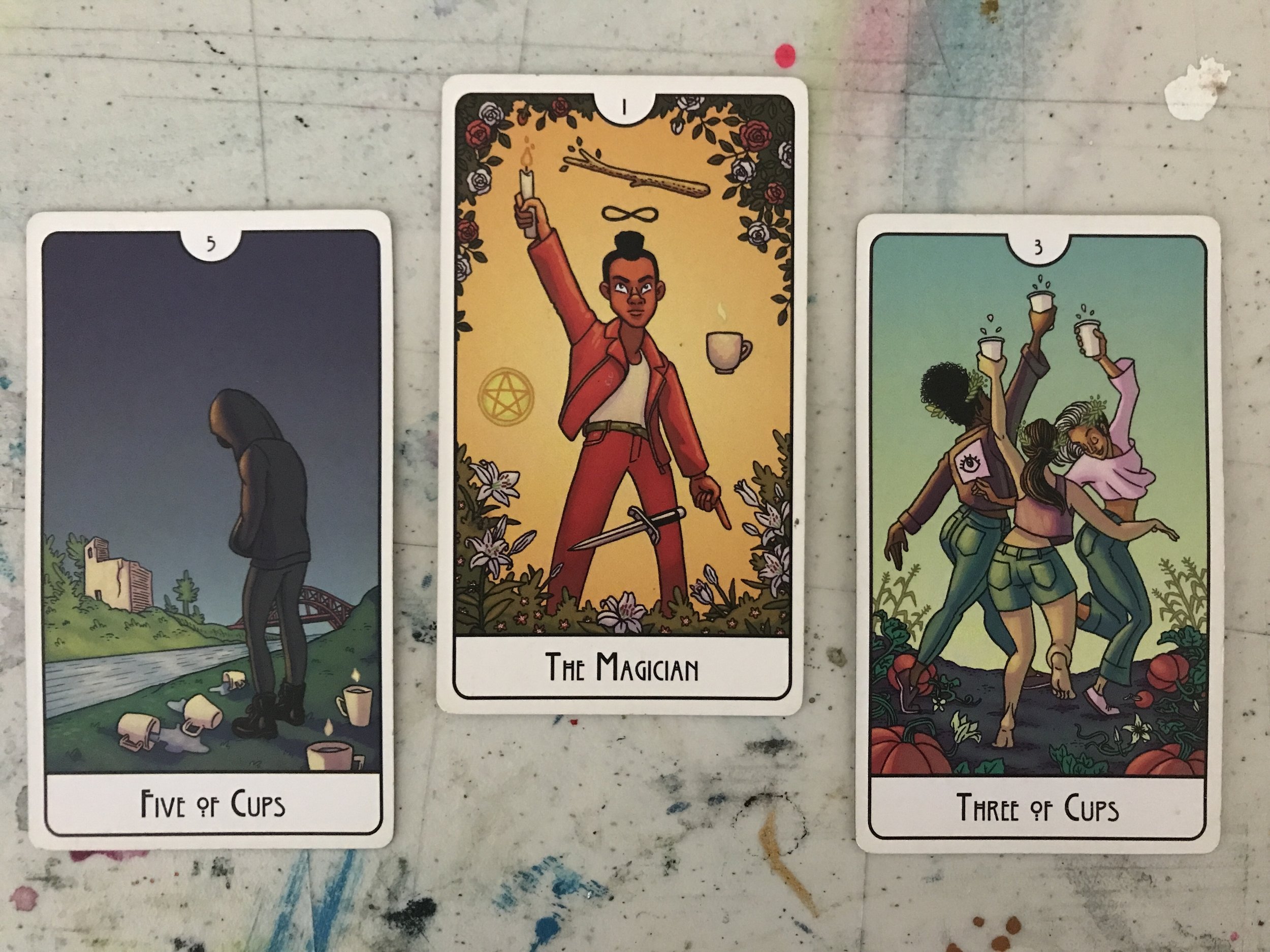 3 tarot cards against a scratched and marked-up plastic table