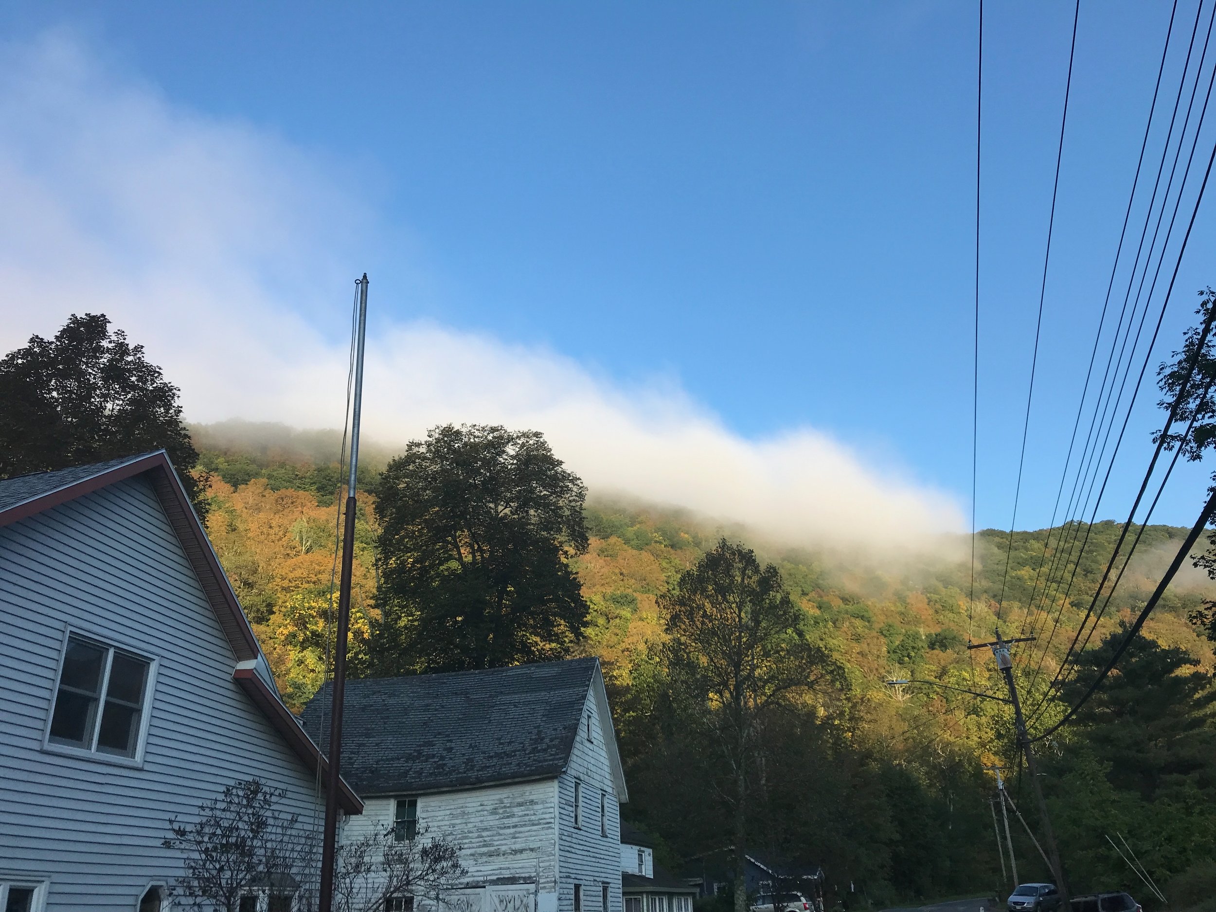 two houses with a mountain in the background, a blue sky, and a strip of clouds against the top of the mountain