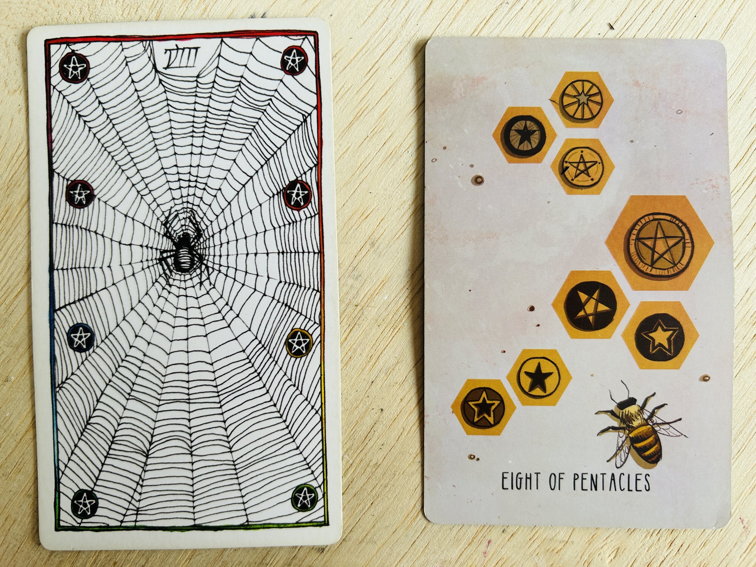 two tarot cards on a light wood surface with diagonal grain