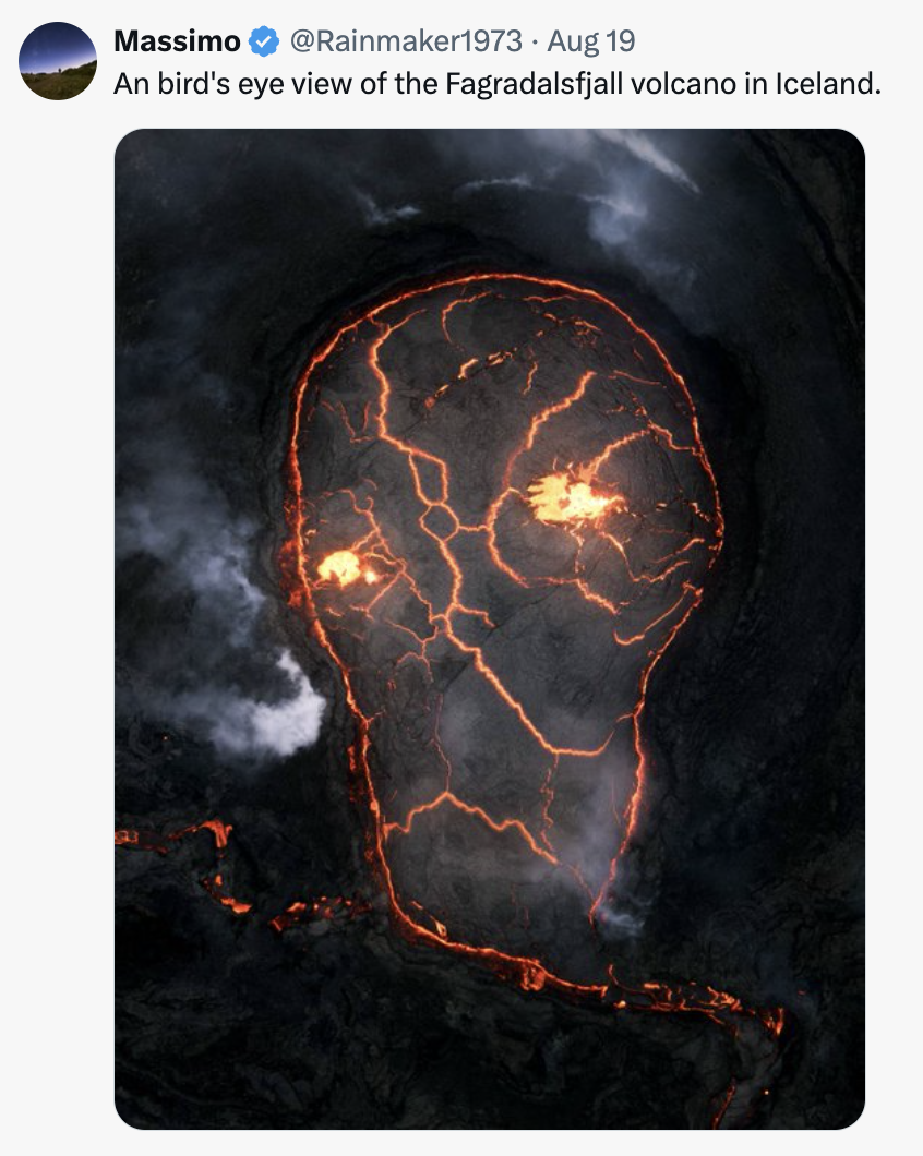 an aerial view of the molten lava of an erupting volcano that looks like a skull with glowing eyes