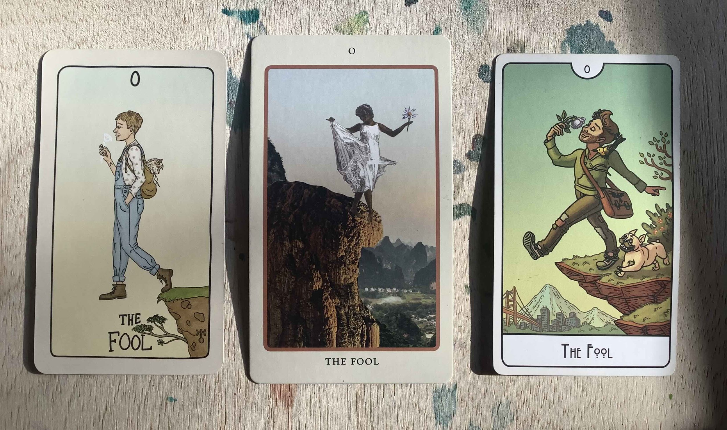 three tarot cards on a paint-splattered wood background