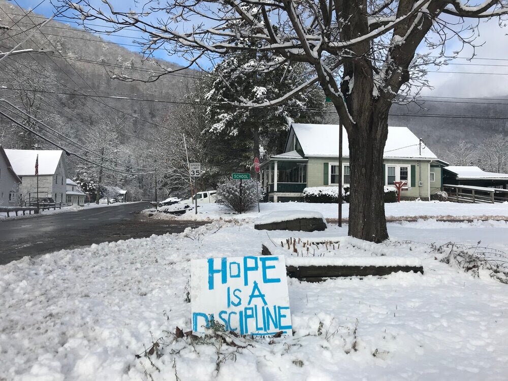 a snow covered neighborhood with a lawn sign that says Hope is a discipline