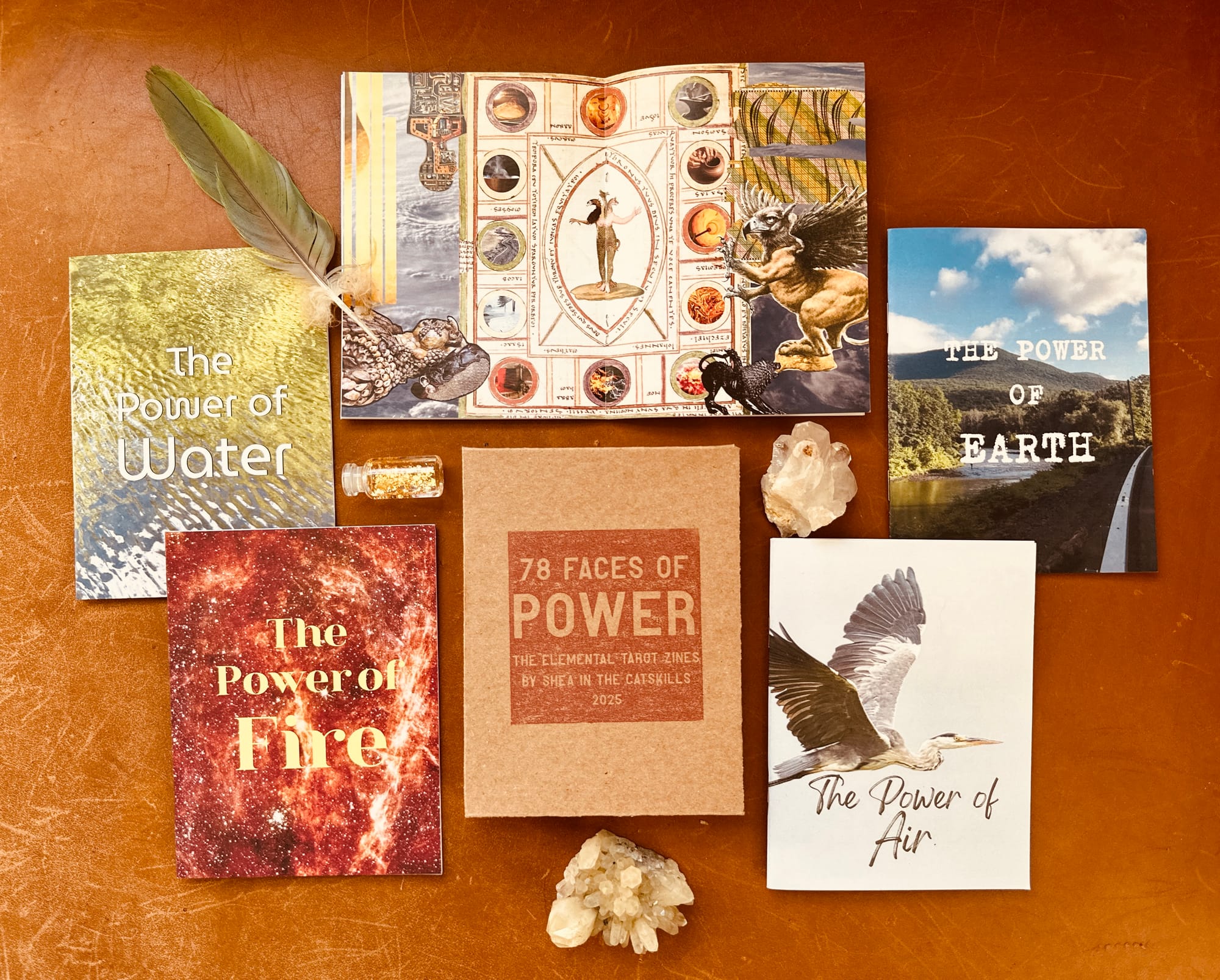 five quarter-page zines arranged against a brown leather ground with crystals and a feather