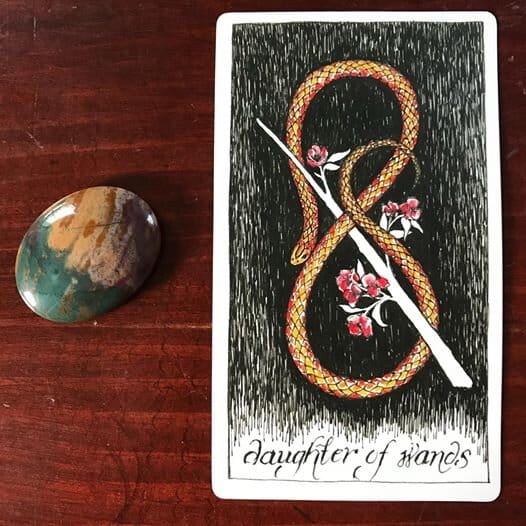 a young orange-pink snake forms their body into a sinuous lemniscate around a diagonal white wand with pink flowers against a black groun