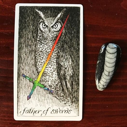 a great horned owl looks directly at the viewer while standing upright on the hilt of an angled rainbow sword