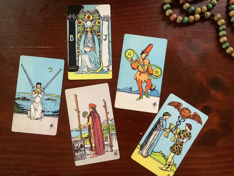 5 tarot cards and colored wooden beads against a dark wood background