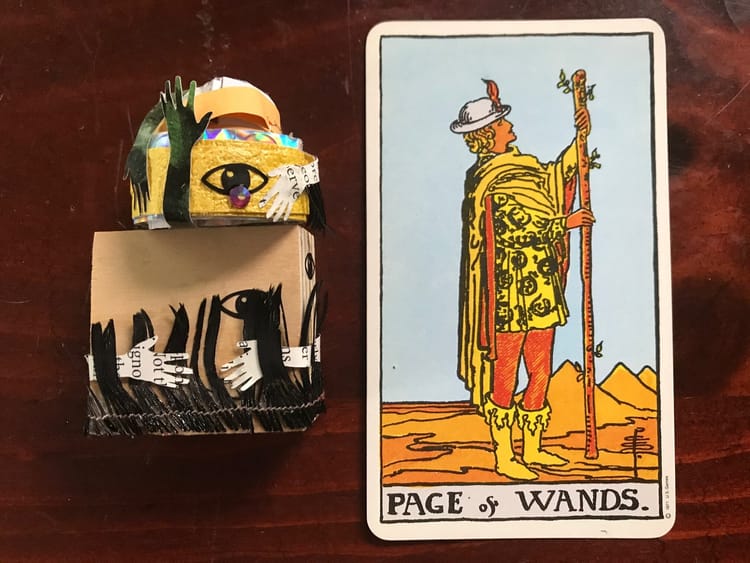 a small sculptural artwork and a tarot card against a dark wood background