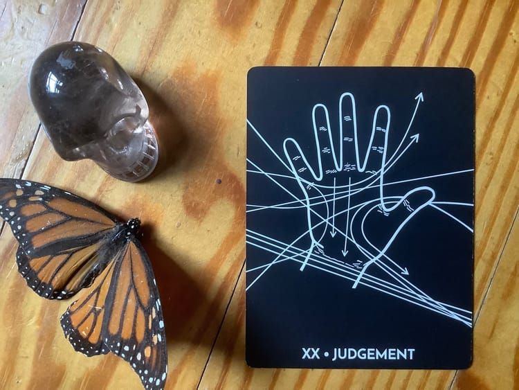 a smoky quartz skull, a dead butterfly and a tarot card against a wood floor