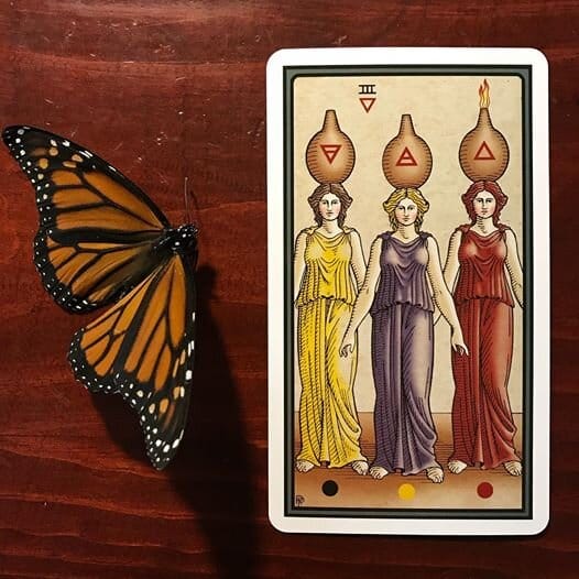three women in yellow, blue and red dresses with bulbous vessels balanced on their heads