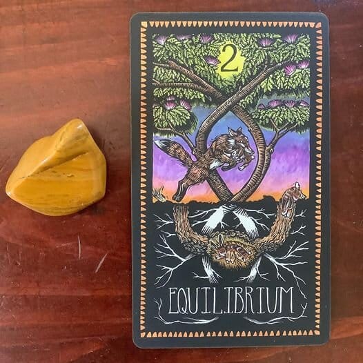 a yellow jasper stone alongside a tarot card depicting a leaping fox and two intertwining trees and the keyword Equilibrium