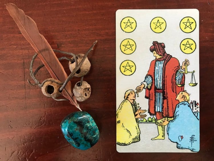 a small pink feather, empty seed pods, a curled twig and a turquoise stone next to a tarot card on a dark wood background