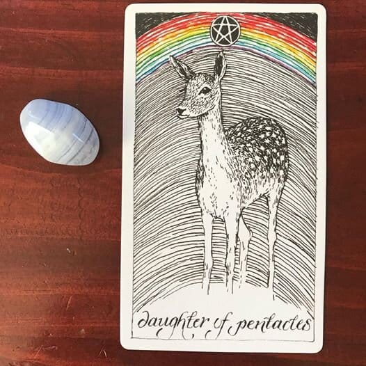 a spotted fawn stands alert against a background of arcing lines with a rainbow at the top and black pentacle hovering in the top center
