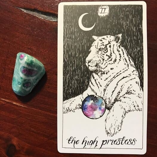 a black-and-white line drawing of a white tiger at rest with a blue purple and black orb between its paws and a write crescent moon above its head