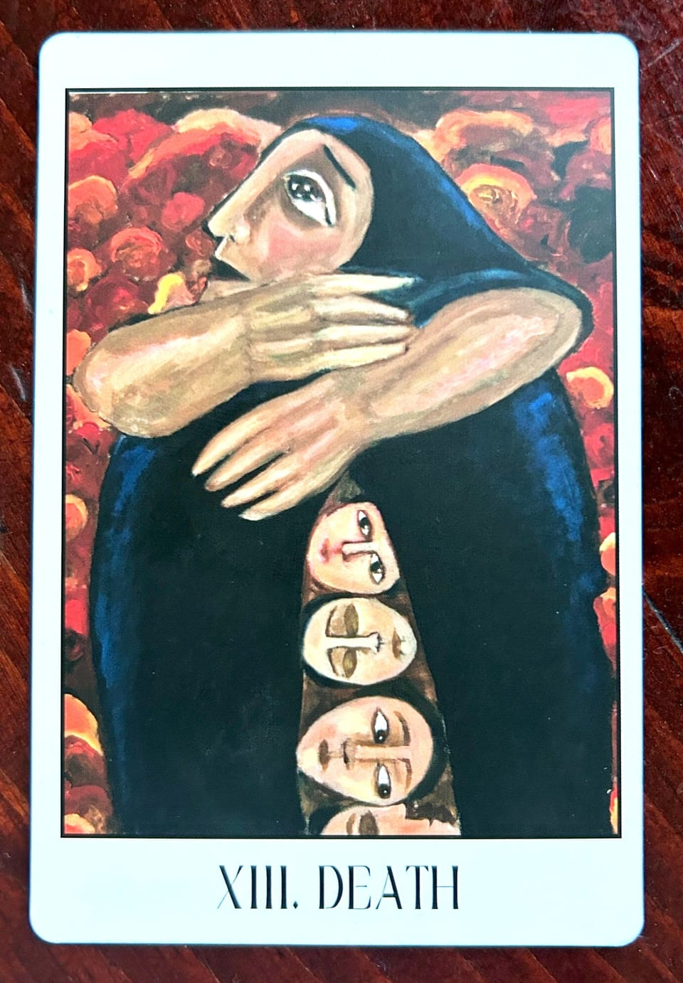 death tarot card showing a crying veiled woman with big arms wrapped around her robe through which several sideways faces appear