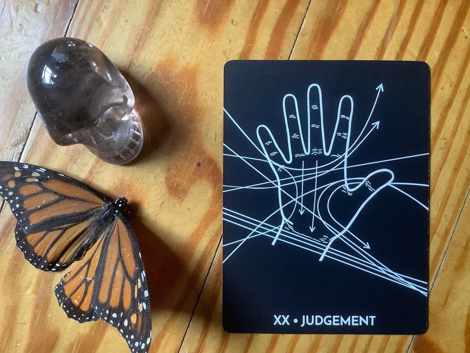 a smoky quartz skull, a dead butterfly and a tarot card against a wood floor