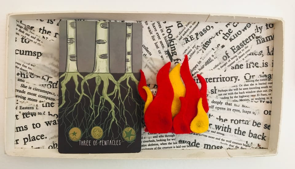 a tarot card inside an artwork of collaged text and flames of red and yellow felt