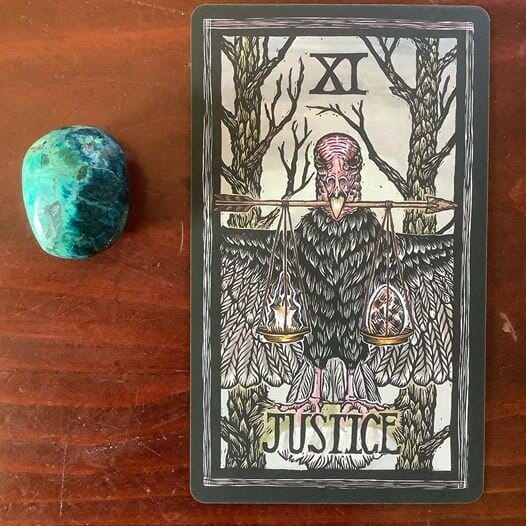 a chrysacholla stone alongside a tarot card showing a turkey vulture with a scale in its beak with a skull on one pan and a heart on the other