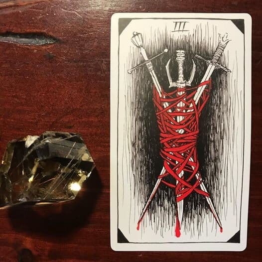 a tarot card showing three swords bound together in a tangle of blood-red ties with blood dripping off the sword tips