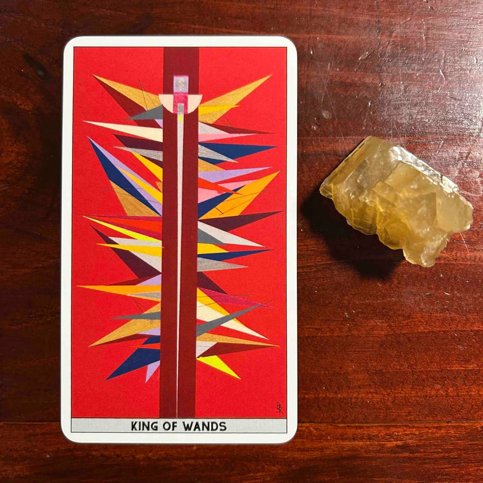 an abstract tarot card with brightly colored spiky shapes forming a central column with a bright tomato red background against a dark wood surface